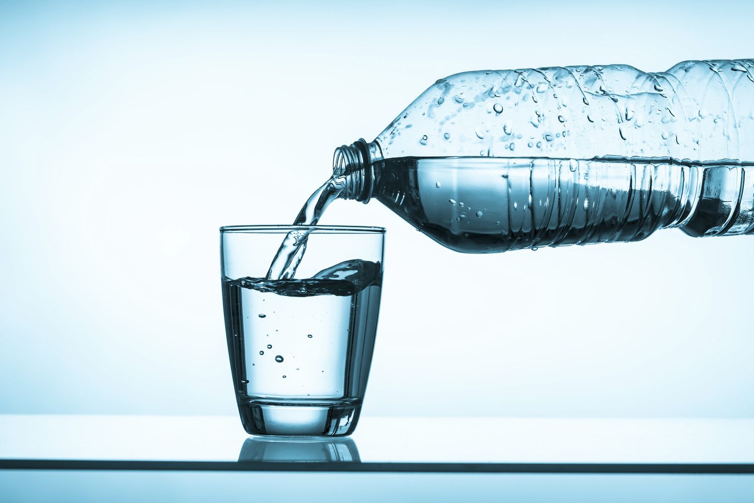 Close-up van water dat vanuit een fles in een glas wordt geschonken.